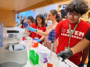 STEM Ambassadors work in a lab pipetting while professors look on