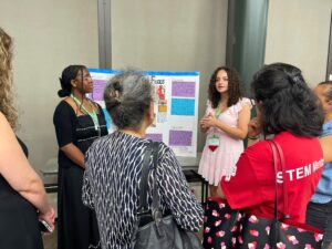 Two STEM Ambassadors present their research project poster to a group gathered around