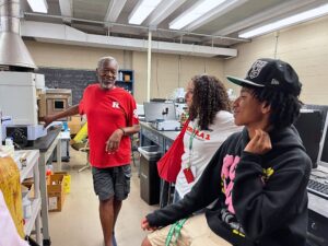 Two Teens look on as a a man in a Rutgers shirt teaches in a lab