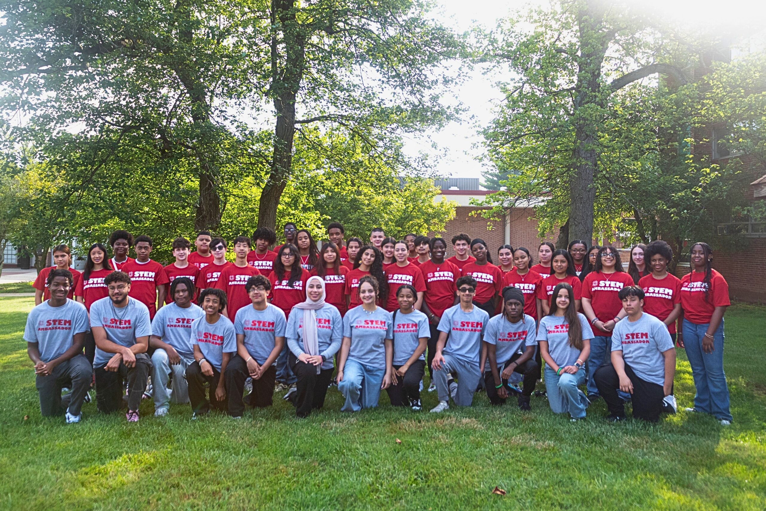 A group of young people wearing STEM Ambassador shirts pose in a grassy area